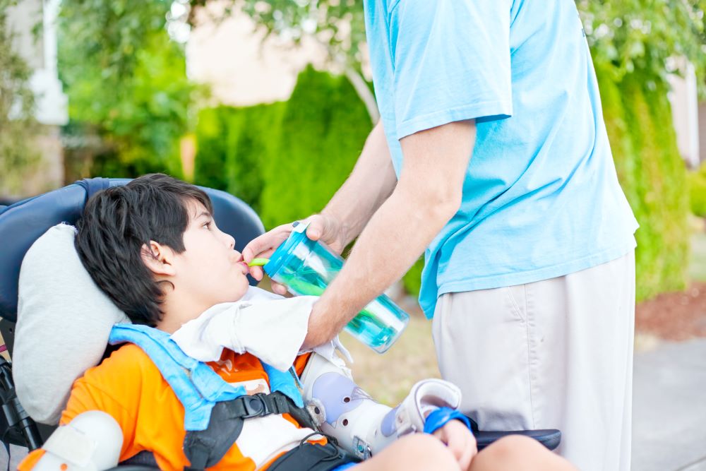 Person helping young boy take a drink from a cup